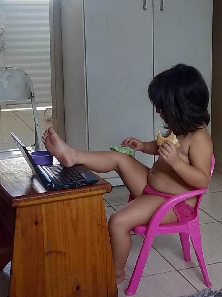 criança sentada em cadeira comendo com pé na mesa