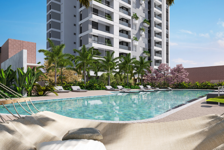 Área de lazer composta por uma piscina, espreguiçadeiras, plantas e vegetações ao redor, e um empreendimento vertical ao fundo.