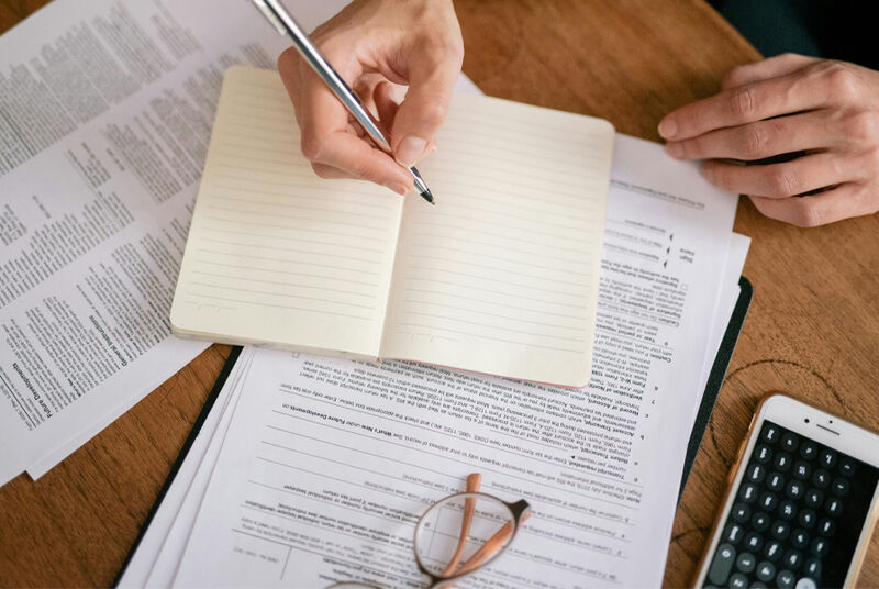 Pessoa escrevendo em caderno sobre documentos