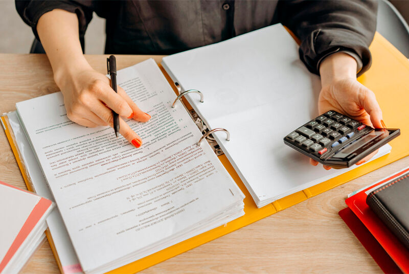 Pessoa analisando documentos com uma calculadora
