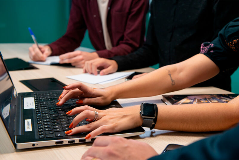 Mãos digitando em laptop durante reunião de trabalho.