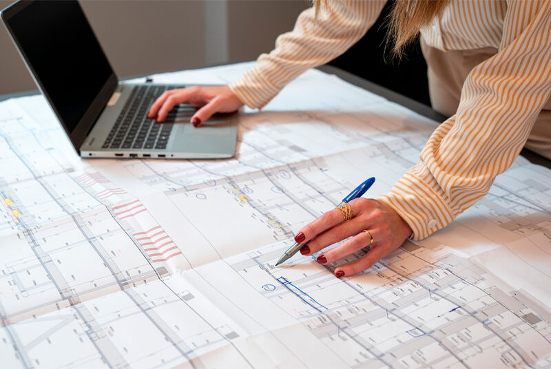 Pessoa analisando planta baixa com laptop e caneta