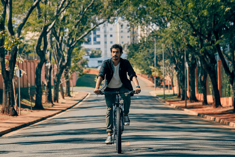 Homem montando bicicleta em rua arborizada