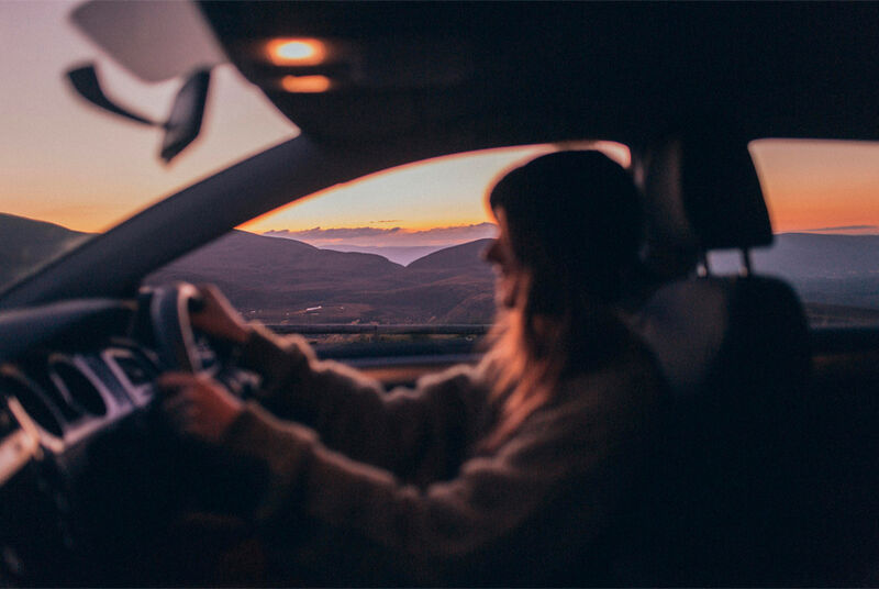 Mulher dirigindo em pôr do sol nas montanhas