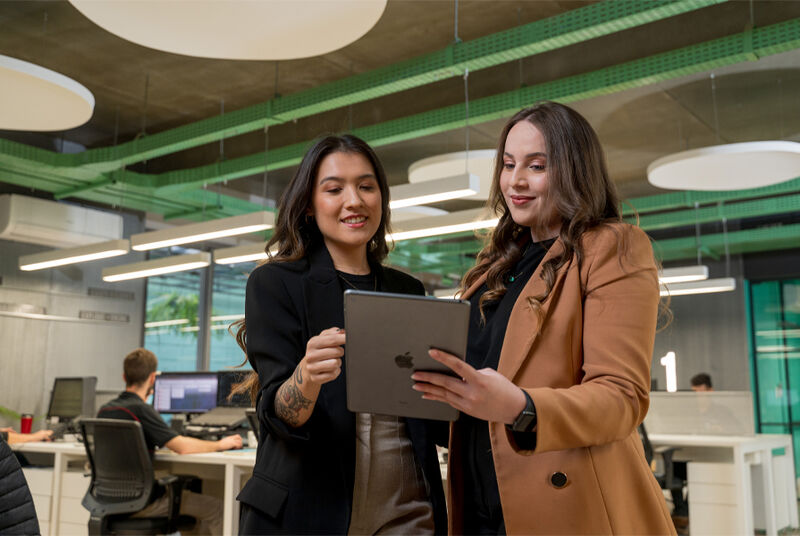 Duas mulheres analisam dados em tablet no escritório moderno.
